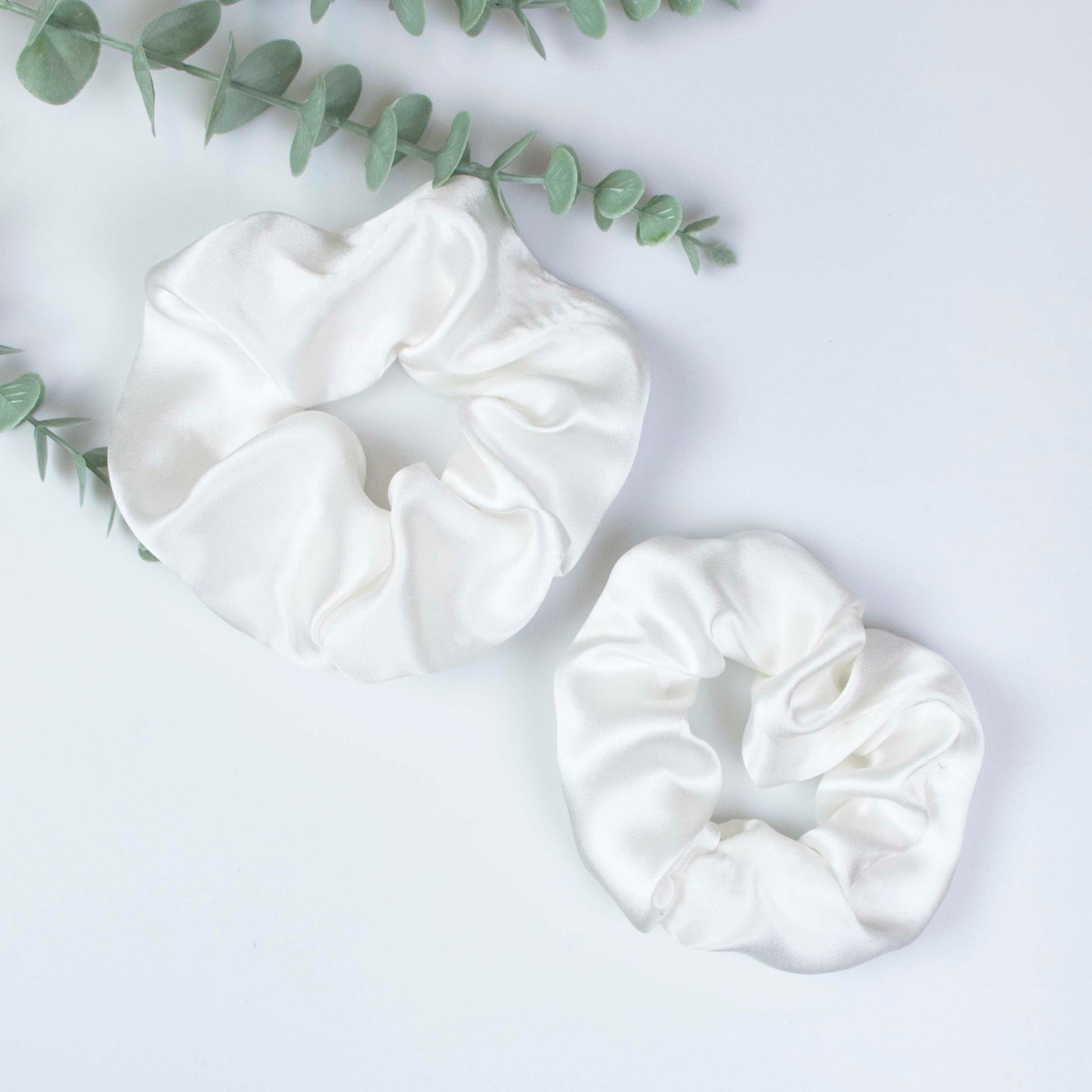 Peace Silk scrunchie natural white – large and small size side by side, eucalyptus sprig, overhead view