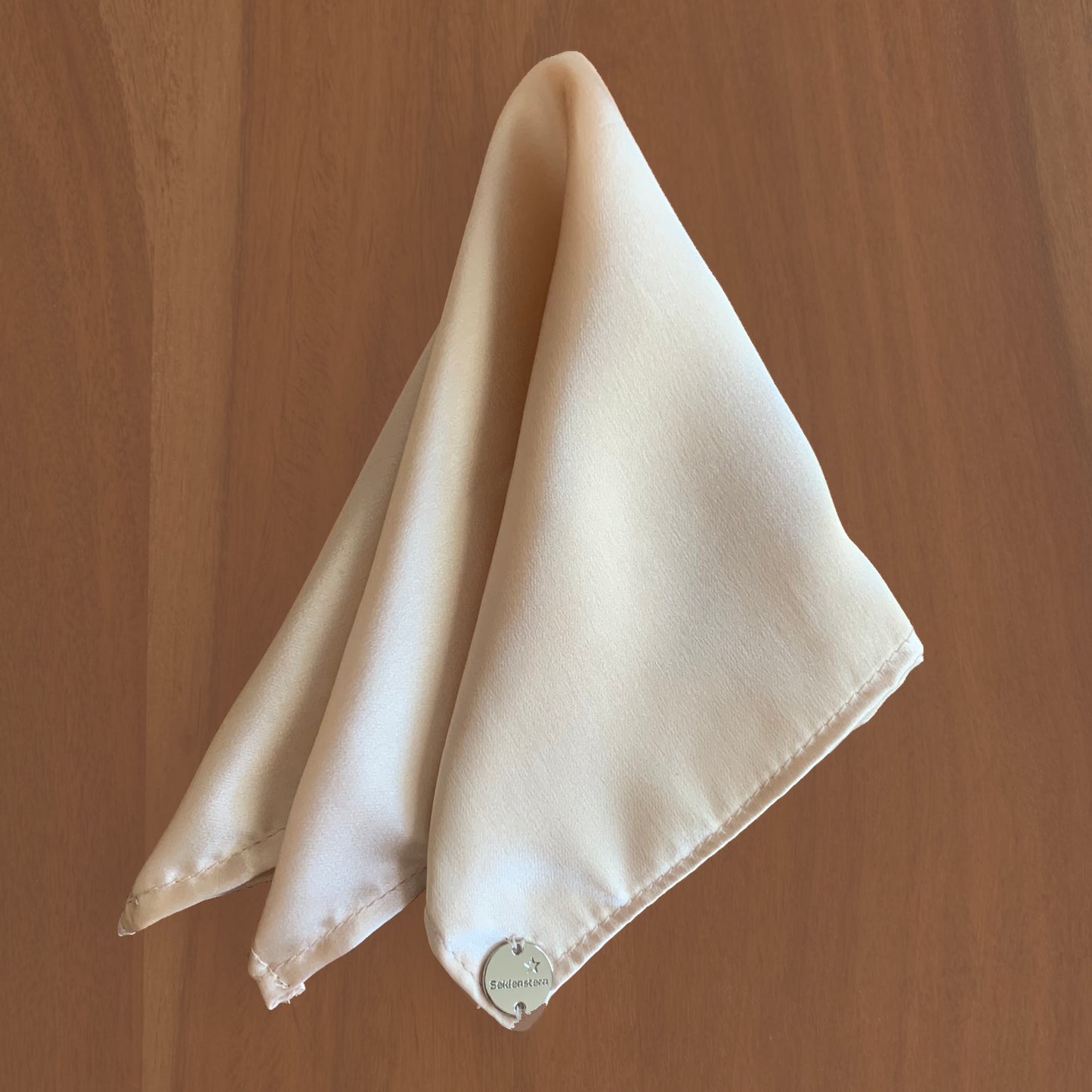 Peace Silk scarf satin beige blush – folded as triangle on wooden surface, top view
