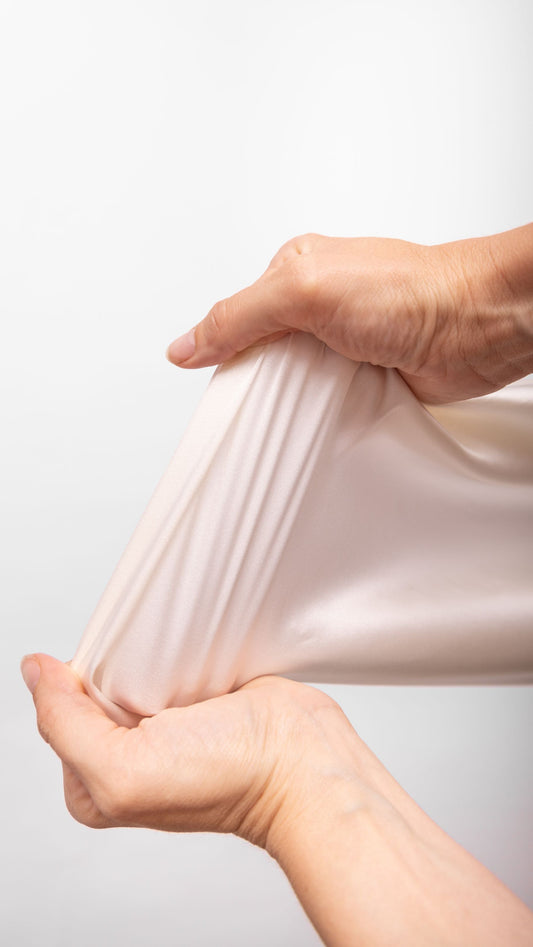 Peace Silk Stretch-Satin Amita – zwei Hände dehnen Stoff auseinander, Stretch-Eigenschaft demonstriert